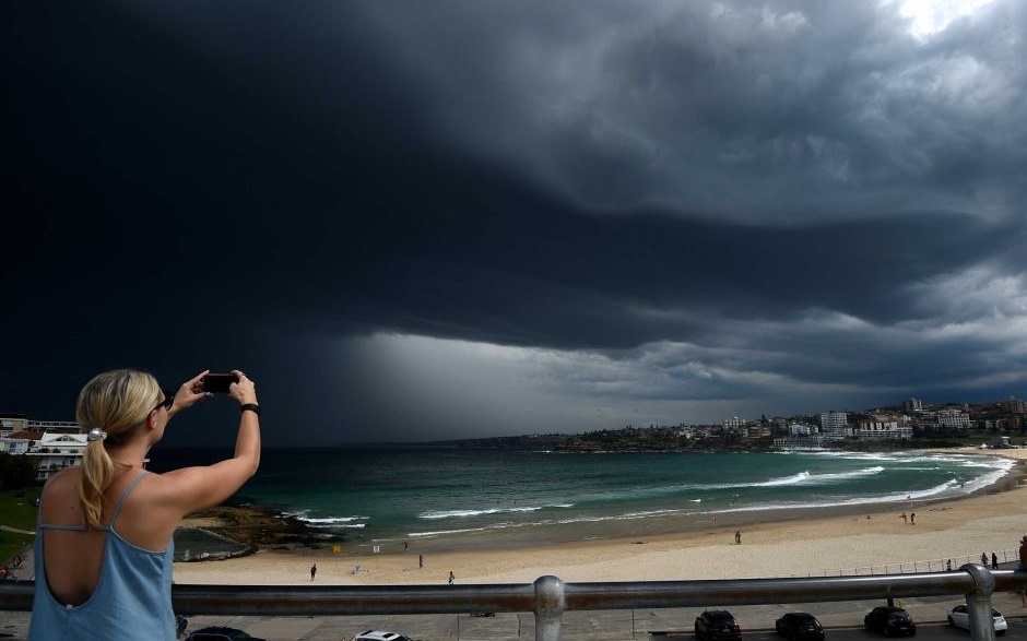 A woman photographs storm clouds over Bondi beach, with the BoM issuing a severe thunderstorm warning for Sydney. AAP Photo: Dan Himbrechts